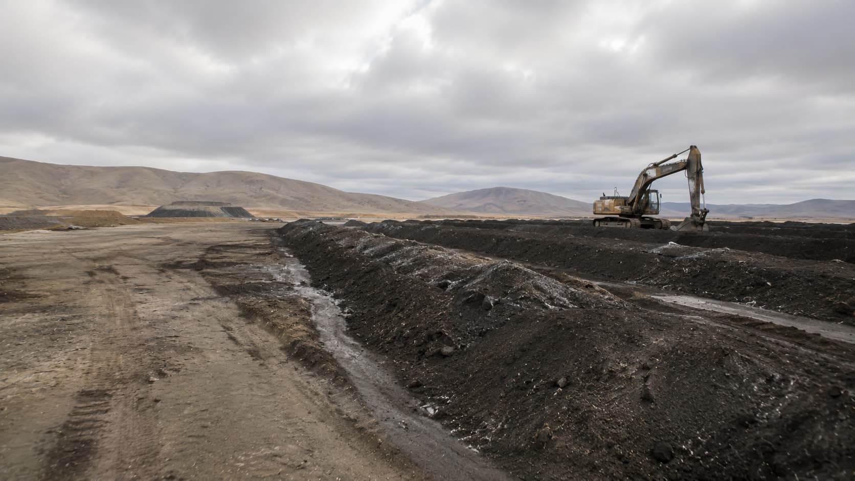 Suelo industrial en proceso de remediación, con maquinaria de movimiento de tierra al fondo.